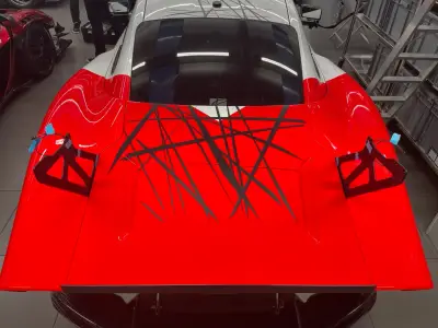 Red Porsche race car front with black abstract slash graphic livery, overhead view