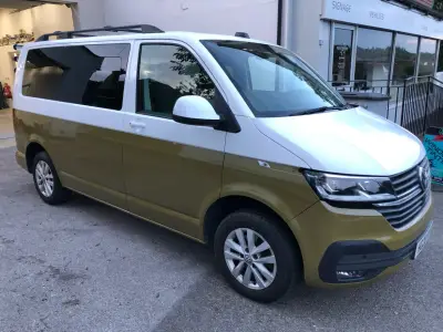 Two-tone white-over-gold VW Transporter van, front side view outside workshop