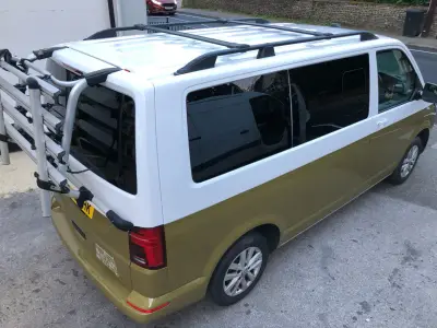 Rear-left of white-and-gold VW Transporter with bike rack and house line graphic