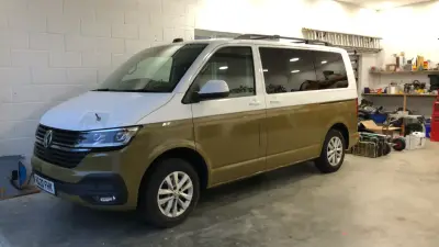 VW Transporter in olive green and white part wrap parked in a workshop