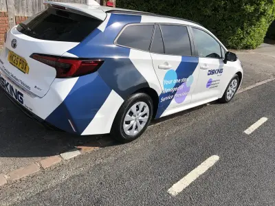 White Toyota Corolla estate with blue geometric DISKING IT part wrap, rear view