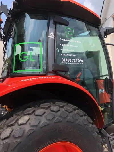 Red Kubota tractor cab with Graduate Landscapes GL logo and service window graphics