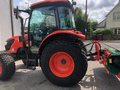 Red Kubota tractor with green Graduate Landscapes window graphics and flail attachment