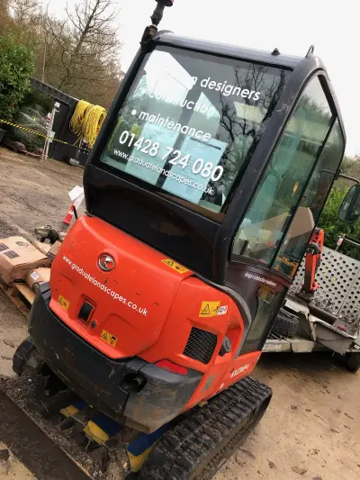 Orange Kubota mini digger with Graduate Landscapes glass graphics on a trailer