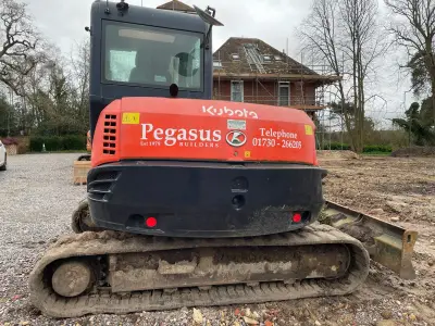Orange Kubota excavator with white 'Pegasus Builders' signwriting on the counterweight at a housebuild