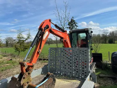 'Pegasus Builders' decal on the boom of an orange Kubota mini excavator loaded on a trailer