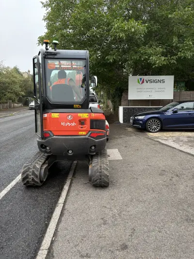 Kubota excavator with 'Spectrum Construction' cab window graphic parked by the VSigns yard sign