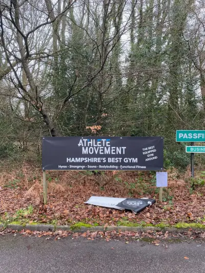 Black 'Athlete Movement - Hampshire's Best Gym' outdoor banner mounted on posts by a roadside