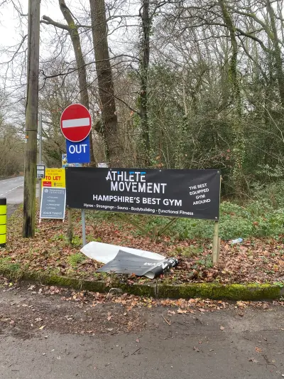 Roadside 'Athlete Movement' gym banner on posts next to an OUT no-entry sign and To Let board