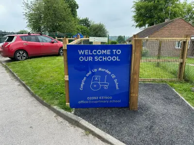 Blue 'Welcome to Our School' sign for Compton and Up Marden CE School by the entrance path
