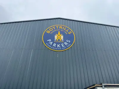 Circular blue and yellow 'Bottrills Parkers' warehouse sign fixed high on grey metal cladding