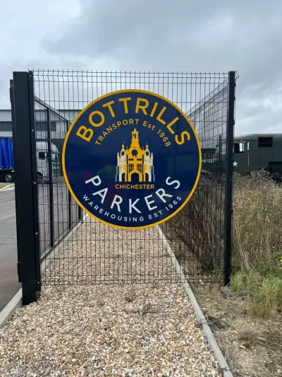 Circular blue and yellow Bottrills Parkers Chichester sign mounted on a mesh entrance gate