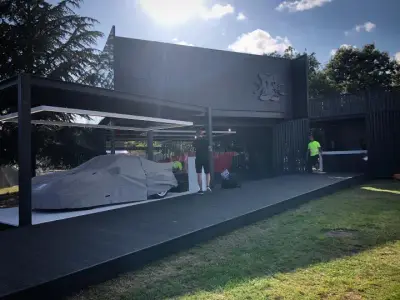 Black Lanzante event pavilion structure with logo, a covered car alongside on decking
