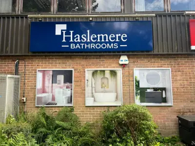 Blue Haslemere Bathrooms fascia sign above three bathroom display panels on brick
