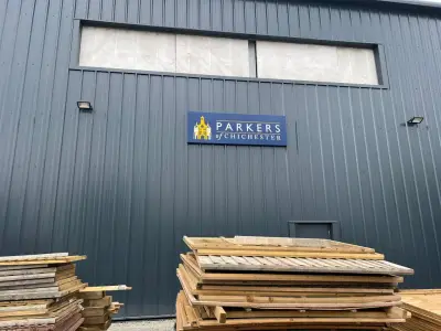 Parkers of Chichester navy fascia sign on a grey warehouse above stacked timber
