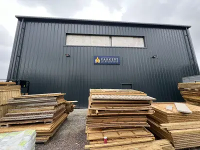 Parkers of Chichester navy sign on a grey warehouse with stacked timber fencing