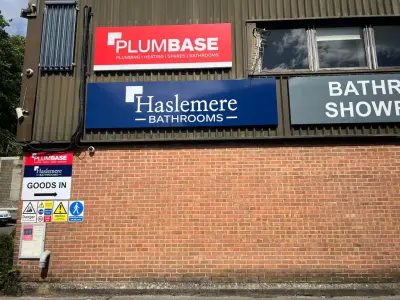 Plumbase and Haslemere Bathrooms fascia signs with a Goods In directional sign on brick