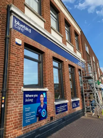 Bluebird Care blue fascia sign and Where You Belong window graphics on brick frontage