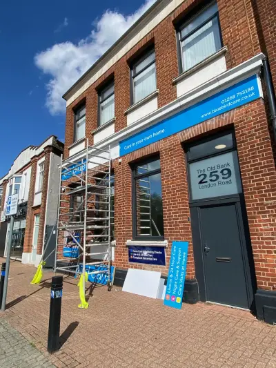 Bluebird Care blue shopfront fascia sign being installed from a scaffold tower on London Road