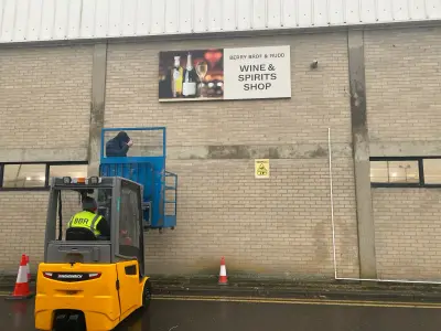 Berry Bros & Rudd Wine & Spirits Shop wall sign being installed from a forklift cage