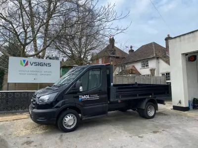 TMGL The Moseley Group black Ford tipper truck with door signwriting beside a V Signs board