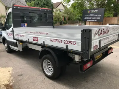 White Ford Transit tipper with maroon Casmin Construction signwriting, V Signs board behind