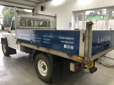 White tipper truck with blue Eavoak dropside signage listing annexes, garages and stables