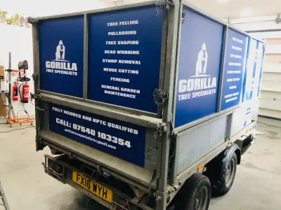 Galvanised tipping trailer with blue Gorilla Tree Specialists service-list signage panels