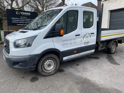 White Ford Transit crew-cab tipper with Arborlec Services signwriting, V Signs board behind