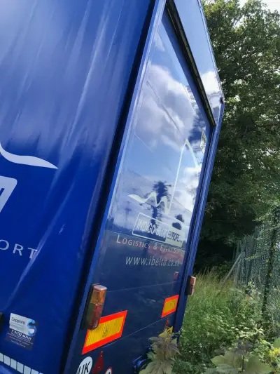 Rear corner of a blue Indigo Blue European curtain-side trailer with logistics graphics