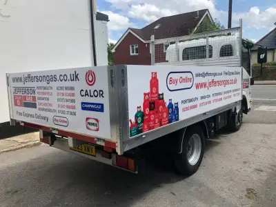 Rear of white Jefferson Gas flatbed showing gas-cylinder graphics and delivery area list