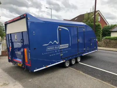 Blue enclosed race car transporter trailer with Indigo Blue European logistics graphics