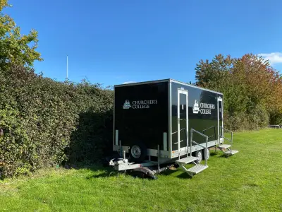 Black mobile toilet trailer with white Churcher's College ship logo graphics on grass