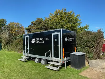 Black mobile shower and toilet trailer with white Churcher's College ship logo