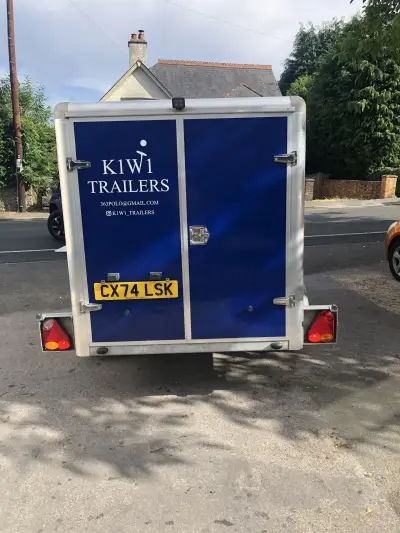 Navy blue enclosed box trailer with white K1W1 Trailers rear door graphics, parked on a street