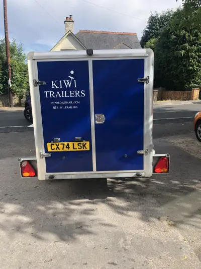 Navy blue enclosed box trailer with white K1W1 Trailers rear door graphics, parked on a street