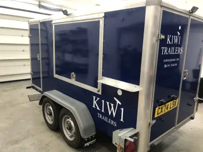 Navy blue K1W1 Trailers enclosed catering trailer, rear three-quarter view with white door and side graphics