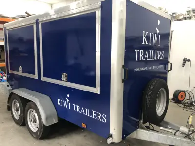 Navy blue K1W1 Trailers enclosed trailer with serving hatches and white signwriting, in a workshop