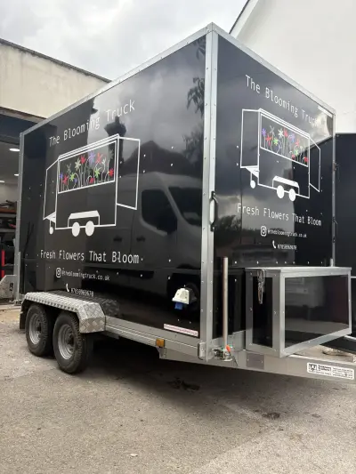 Black box trailer wrapped for The Blooming Truck, front corner showing flower graphics on both sides