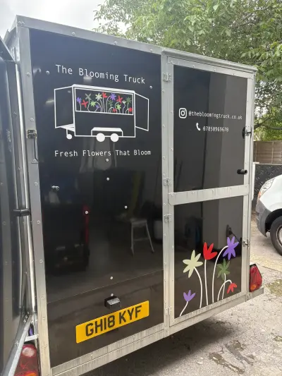 Black box trailer wrapped for The Blooming Truck, rear corner with flower graphics and website details
