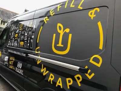 Black van with yellow Refill Unwrapped graphics, a mobile refill store with eco product illustrations