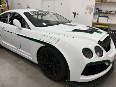 White Bentley Continental GT race car with green stripe motorsport livery, in a workshop