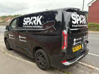 Black Ford Transit Custom van with white SPARK Private Electrical Installation graphics, side view