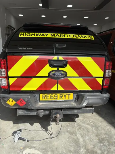 Black Ford Ranger pickup with red and yellow chevron tailgate and Highway Maintenance graphics