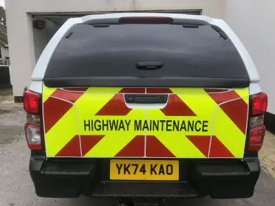 White pickup rear with red and yellow reflective chevrons and Highway Maintenance signwriting