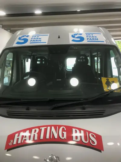 White Peugeot minibus front with 'the Harting Bus' bonnet graphic and Sky Park Farm banners