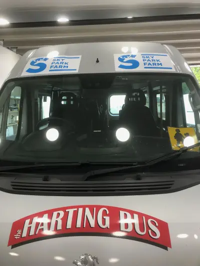 White Peugeot minibus front with 'the Harting Bus' bonnet graphic and Sky Park Farm banners
