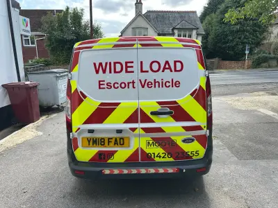 White Ford Transit Custom rear with red and yellow chevrons and Wide Load Escort Vehicle graphics for Moore