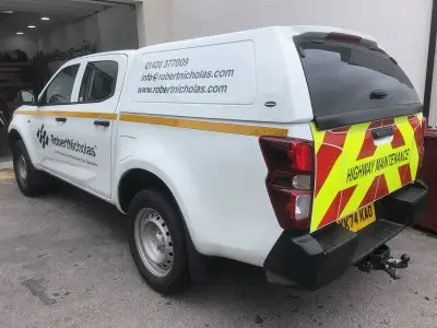 White Isuzu pickup with Robert Nicholas graphics and Highway Maintenance chevron rear panel