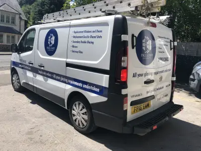White Vauxhall Vivaro van signwritten for Paul Gard Glass & Glazing, rear three-quarter view with roof ladders